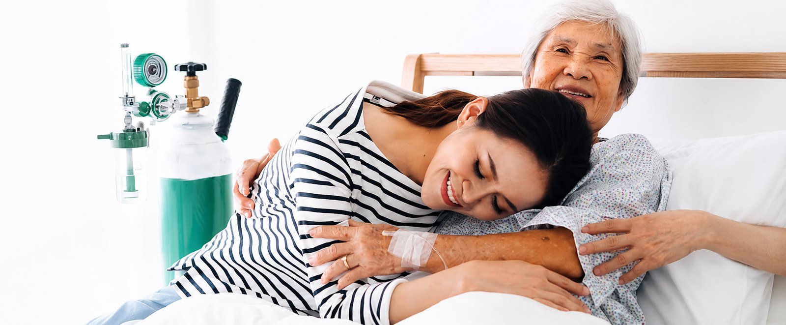 Coach de Vida y Empresarial PNL 16 Mujer joven abrazando con cariño a una adulta mayor en una cama de hospital, transmitiendo apoyo emocional, amor y cuidado durante un proceso de salud.